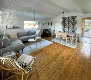 A cozy living room with a sofa, two round tables, a dining table with chairs, a fireplace, and a large abstract wall art piece. - House by a secluded lake in rural Blekinge (Hallabro)