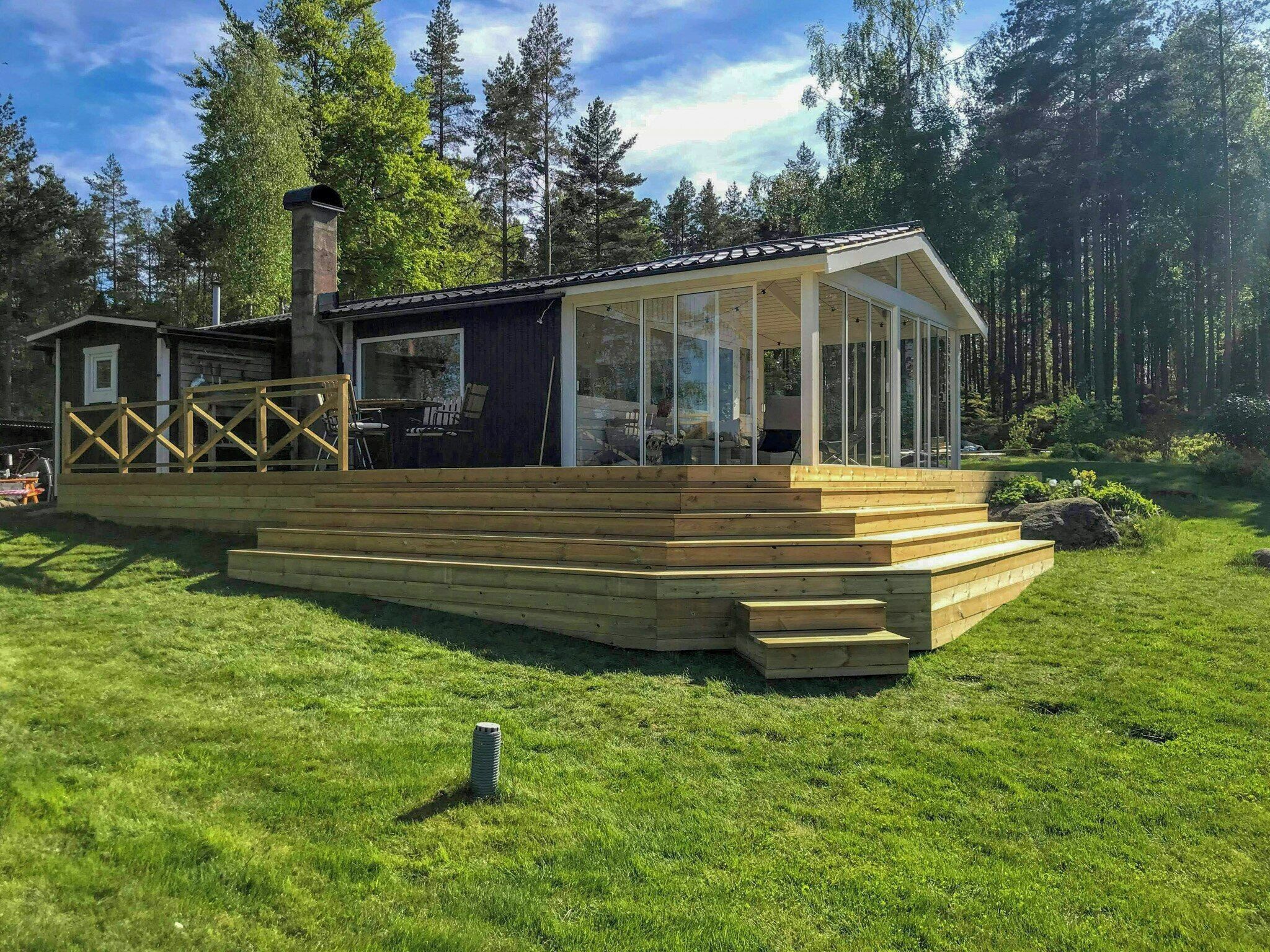 A wooden deck with a glass enclosure, a chimney, and a small building with a white door.