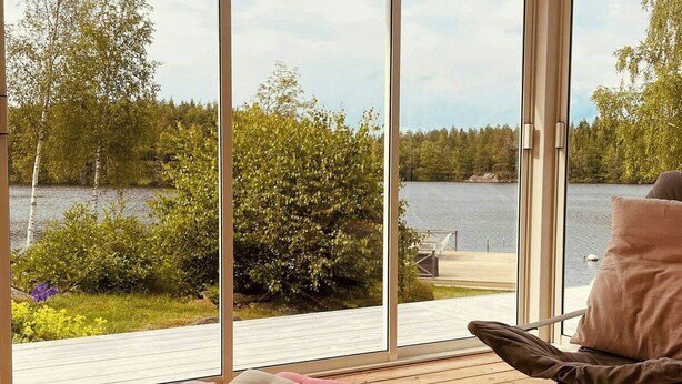 A room with large windows, a table with glasses of wine, and a chair with cushions. - House by a secluded lake in rural Blekinge (Hallabro)