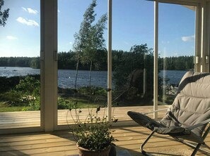 A wooden deck with a chair, a potted plant, and a view of a lake with trees and a dock. - House by a secluded lake in rural Blekinge (Hallabro)