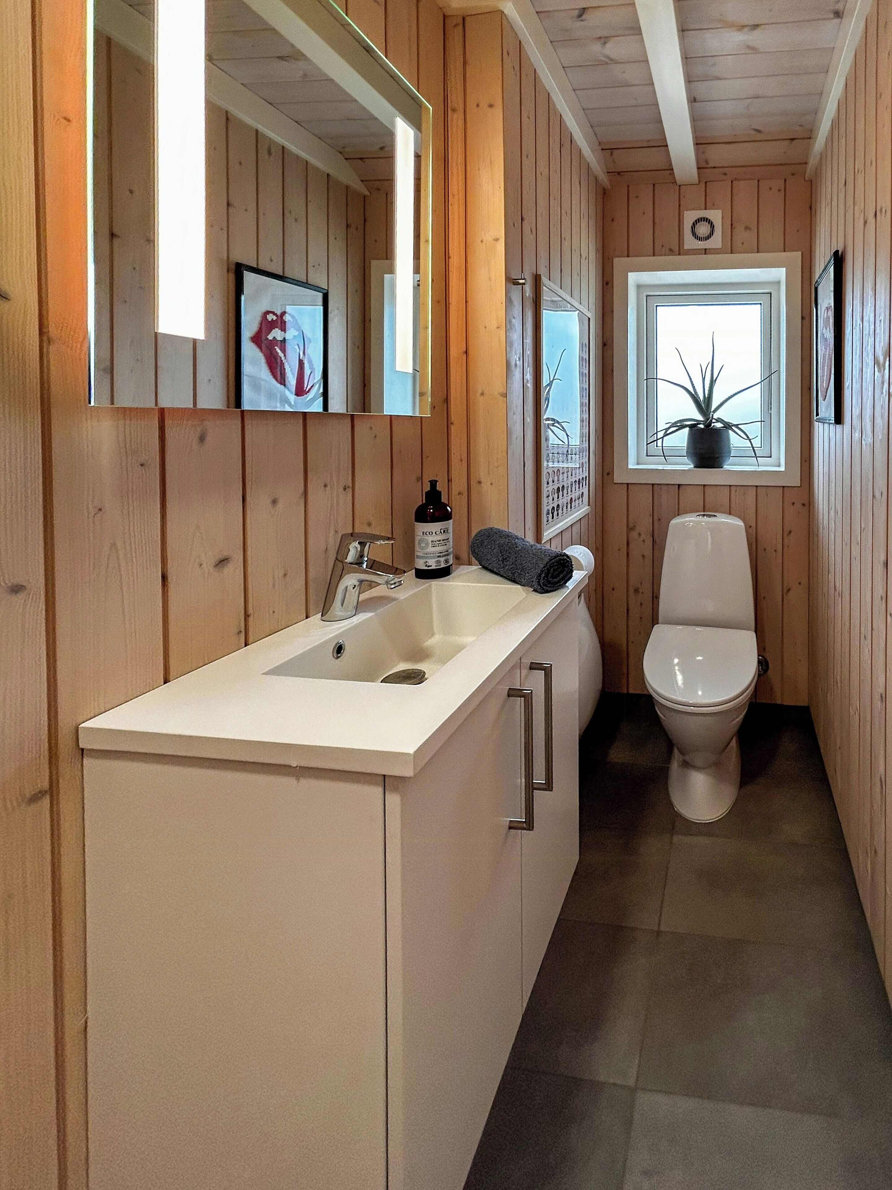 Un bagno con pareti in legno, un lavandino bianco, un water e una finestra con una pianta.