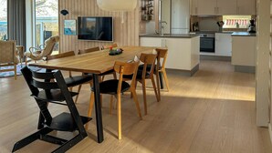 Une cuisine moderne avec des meubles en bois, un coin repas avec une table et des chaises en bois, un téléviseur fixé au mur et un luminaire suspendu.