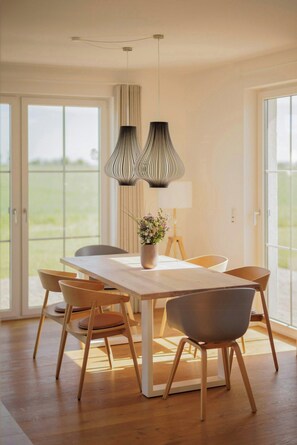 Ein stilvoller Essbereich mit Holztisch, zwei Stühlen, einer Blumenvase und Pendelleuchten.