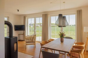 Ein modernes Wohnzimmer mit großem Fenster, Kamin, Esstisch und Fernseher.