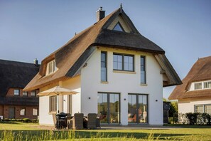 Ein modernes Haus mit einem steilen Dach, großen Fenstern und einer Terrasse mit Gartenmöbeln.