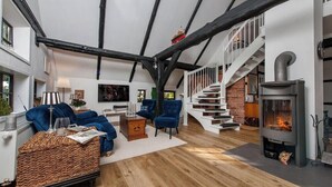Un vaste salon doté d’un haut plafond, de poutres apparentes, d’une cheminée et d’un escalier menant à l’étage supérieur.