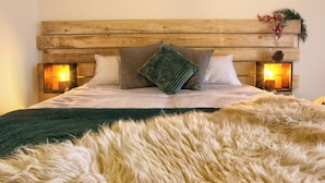 Un letto con testiera in legno, due lampade fissate al muro e una coperta bianca e soffice.