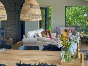 A modern living room with a white sofa, wicker pendant lights, a glass vase with flowers, and a wooden dining table. - Holiday home with panoramic view of Aarhus Bay (Knebel)