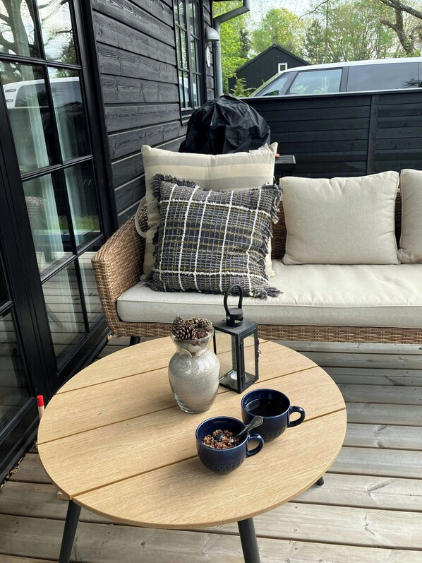 A round wooden table with a vase and two cups on a deck.