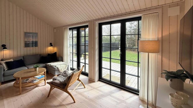 A room with a sofa, a chair, a table, and a large window. - Modern wooden house built in a classic style (Glesborg)