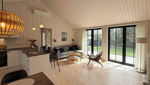 A spacious living area with a large window, a dining table, and a kitchen area with wooden paneling. - Modern wooden house built in a classic style (Glesborg)