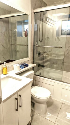 Un bagno con doccia vetrata, un water, un lavandino con specchio e uno scaffale con articoli da toilette.