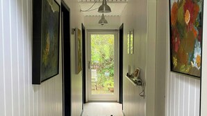 Un pasillo con piso de madera, paredes blancas con paneles y una puerta que da a un jardín.