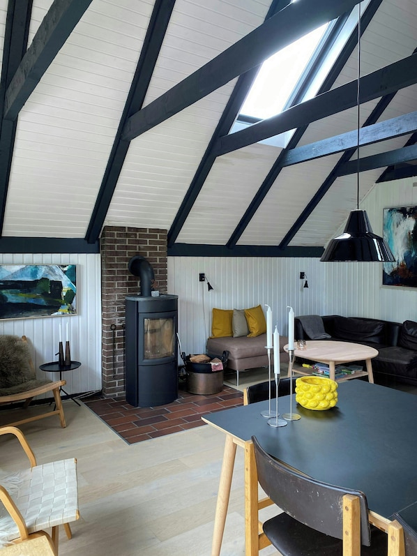 Una sala de estar acogedora con chimenea, un sofá, una mesa de comedor y un amplio ventanal.