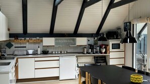 Una cocina moderna con tragaluz, vigas de madera, armarios blancos y un comedor con mesa negra y sillas de madera.