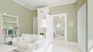 A room with a white sofa, a white table, a bookshelf, and a door leading to another room. - Converted school in Östergötland oak landscape (Tjällmo)