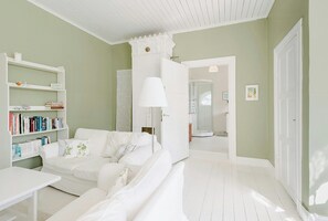 A room with a white sofa, a white table, a bookshelf, and a door leading to another room. - Converted school in Östergötland oak landscape (Tjällmo)