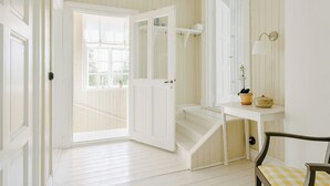 A room with a white door, a white bench, a white table with a potted plant, and a white wall with a light fixture. - Converted school in Östergötland oak landscape (Tjällmo)