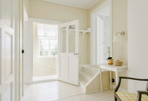 A room with a white door, a white bench, a white table with a potted plant, and a white wall with a light fixture. - Converted school in Östergötland oak landscape (Tjällmo)