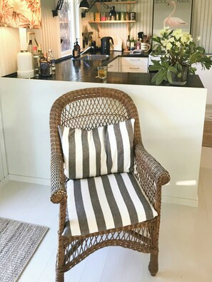A wicker chair with a striped cushion in a room with a kitchen in the background. - Summerhouse by Tisvilde Hegn forest (Tisvildeleje)