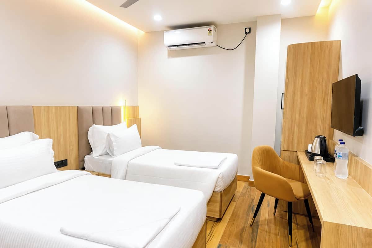 Una habitación de hotel con dos camas, un escritorio con silla, un televisor y un equipo de aire acondicionado.