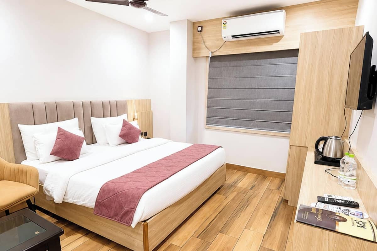 Habitación de hotel con cama, escritorio, silla, ventilador de techo, aire acondicionado y televisor.