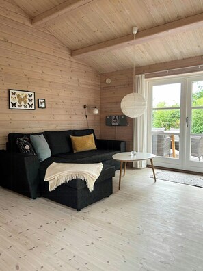 Ein Holzinnenraum mit einem schwarzen Sofa, einem weißen Tisch und einem großen Fenster.