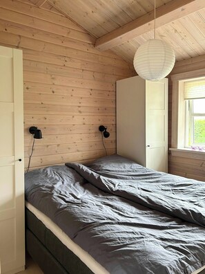 Ein Schlafzimmer mit Holzboden, einem Bett mit grauem Bettzeug, zwei schwarzen Wandlampen und einem weißen Kleiderschrank.