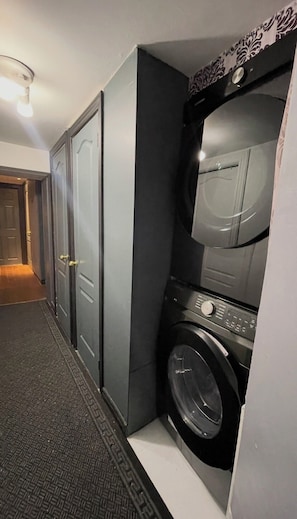A compact laundry room with a front-loading washer and dryer, a door with a key lock, and a patterned wall.