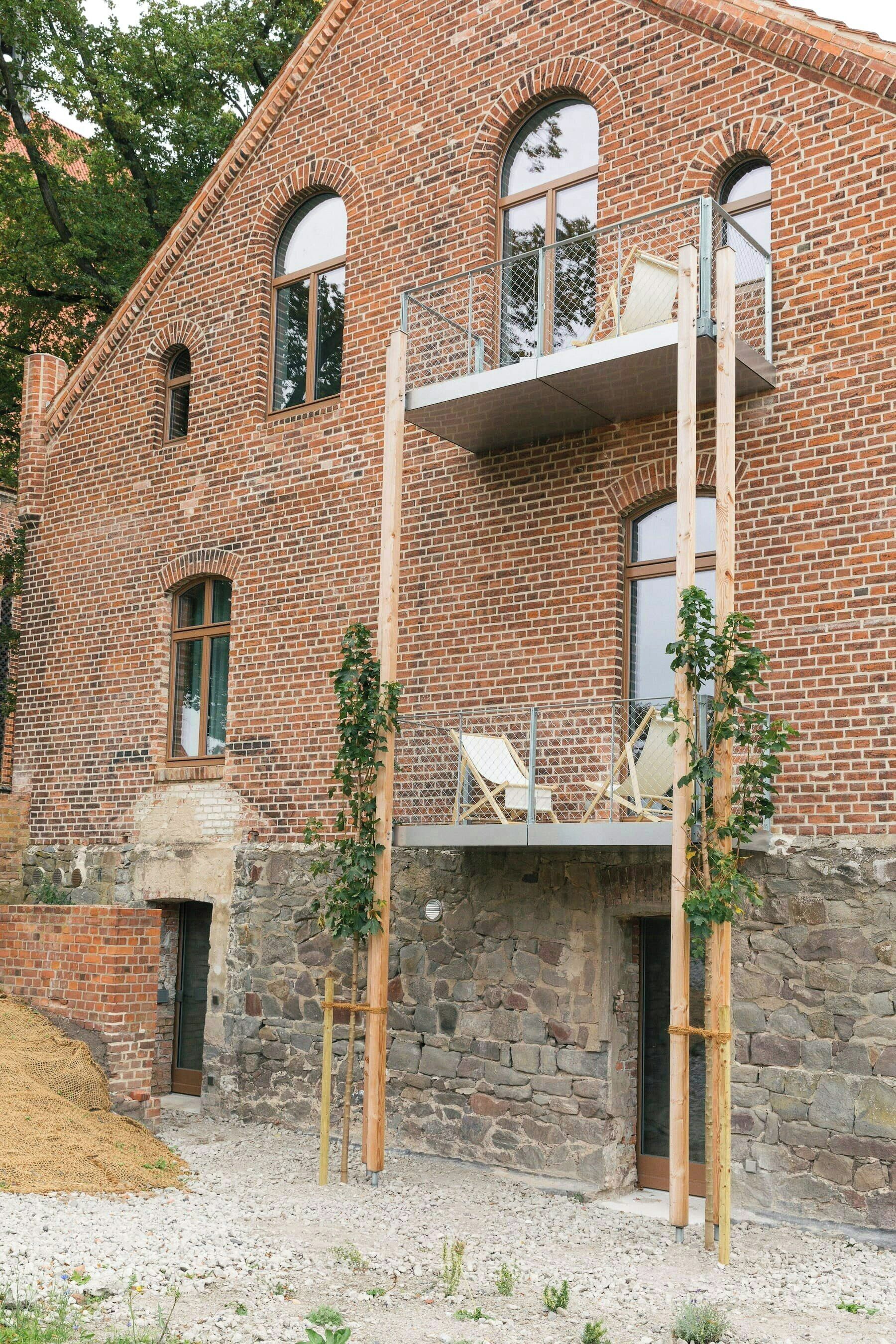 Un bâtiment en briques doté d’un balcon, d’une fondation en pierre et d’une structure en bois à l’avant.