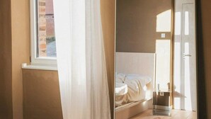 Une chambre avec un grand miroir, un lit, une fenêtre avec des rideaux et un plancher en bois.
