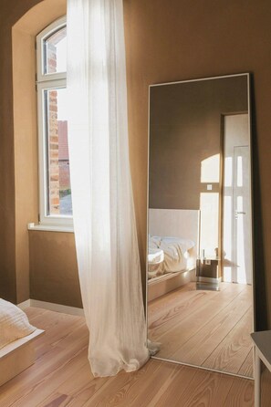 Ein Schlafzimmer mit großem Spiegel, einem Bett, einem Fenster mit Vorhängen und Holzboden.