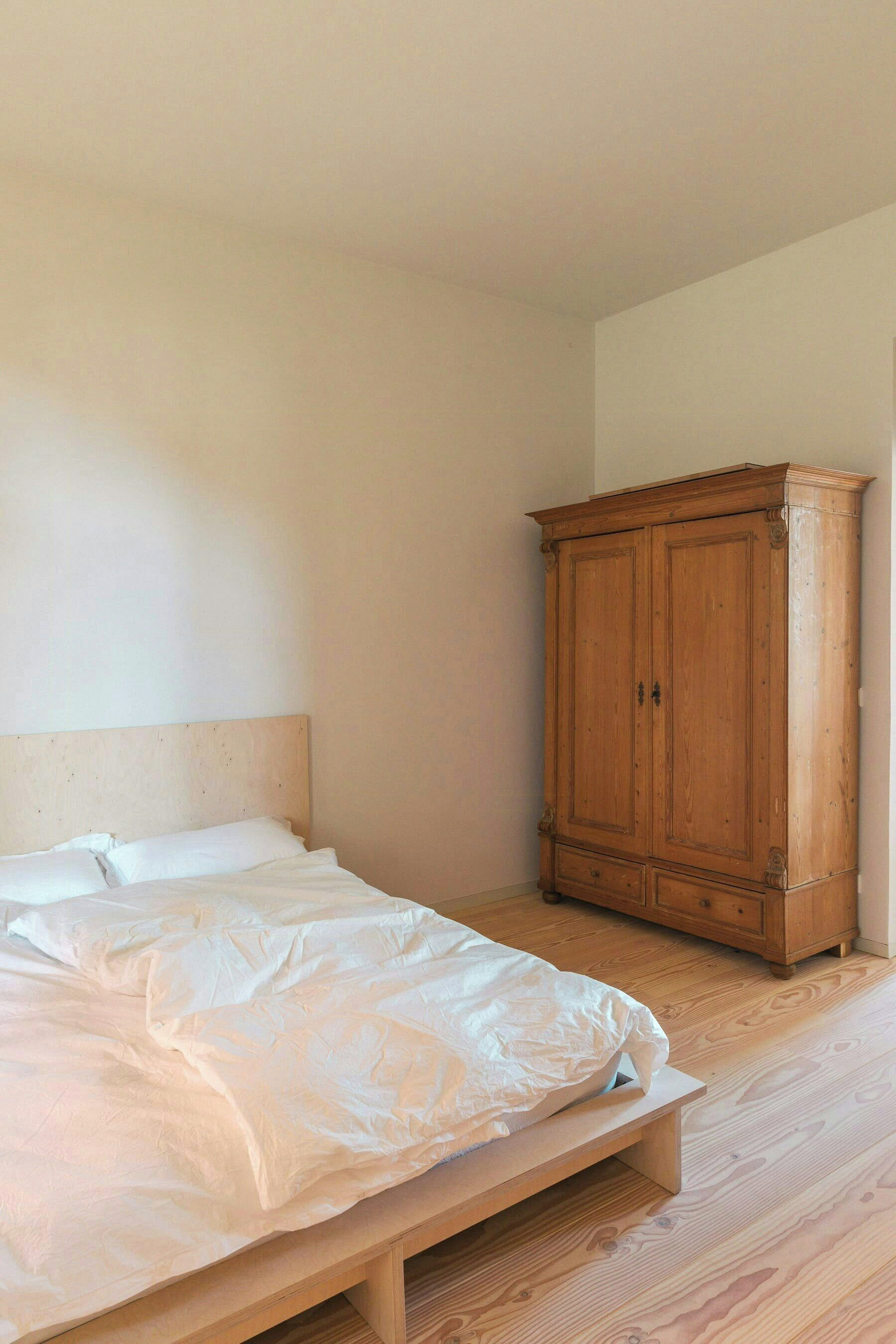 Une chambre à coucher avec un lit en bois, une armoire en bois et un mur uni.