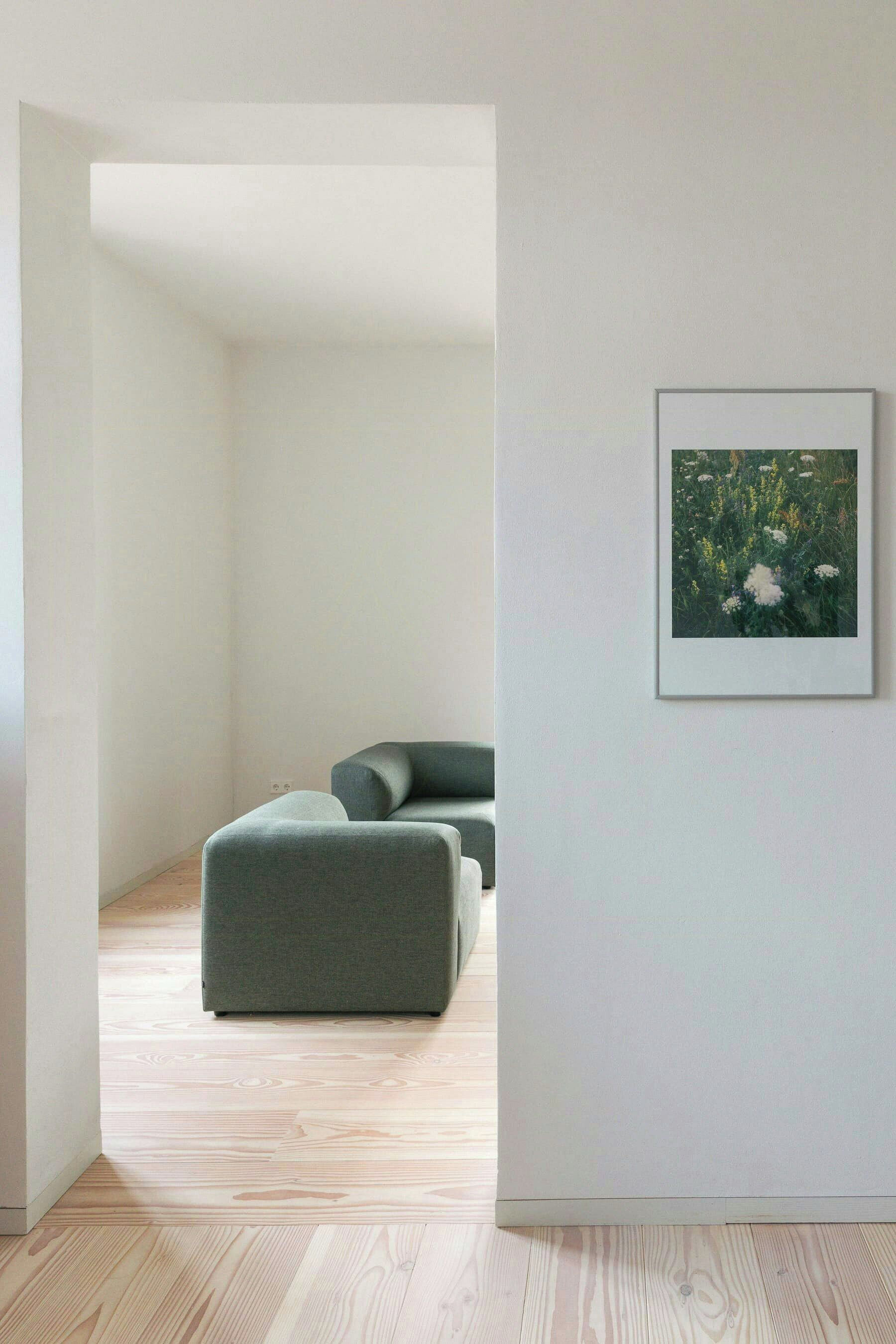 A minimalist room with a wooden floor, a grey sofa, and a framed picture on the wall.