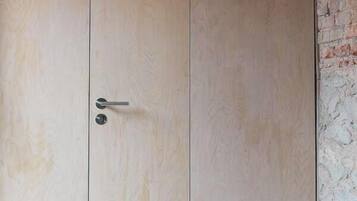 A wooden wardrobe with a door and a small circular vent on the wall.