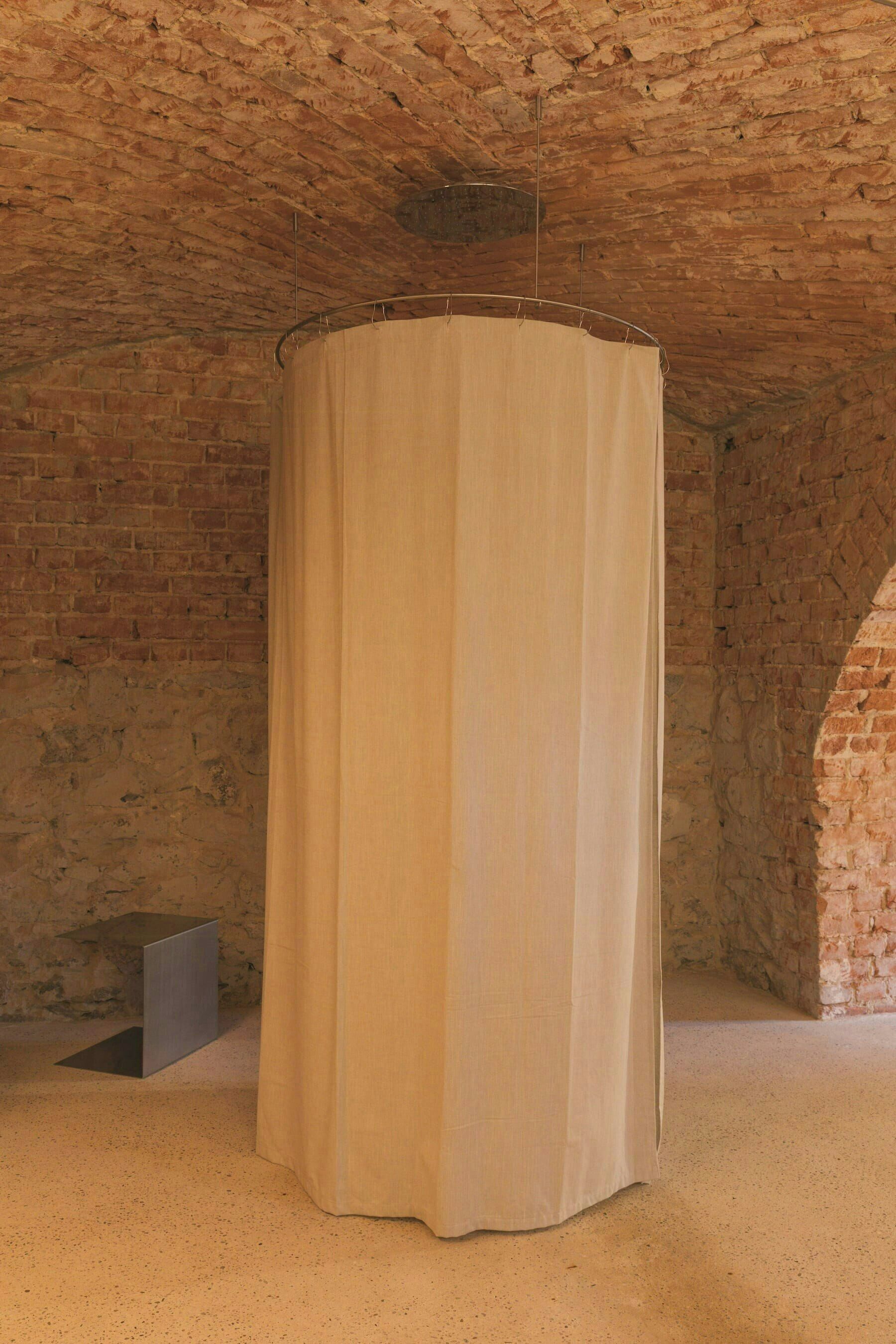 Une pièce avec un mur en briques, un rideau circulaire et un petit objet sombre sur le sol.