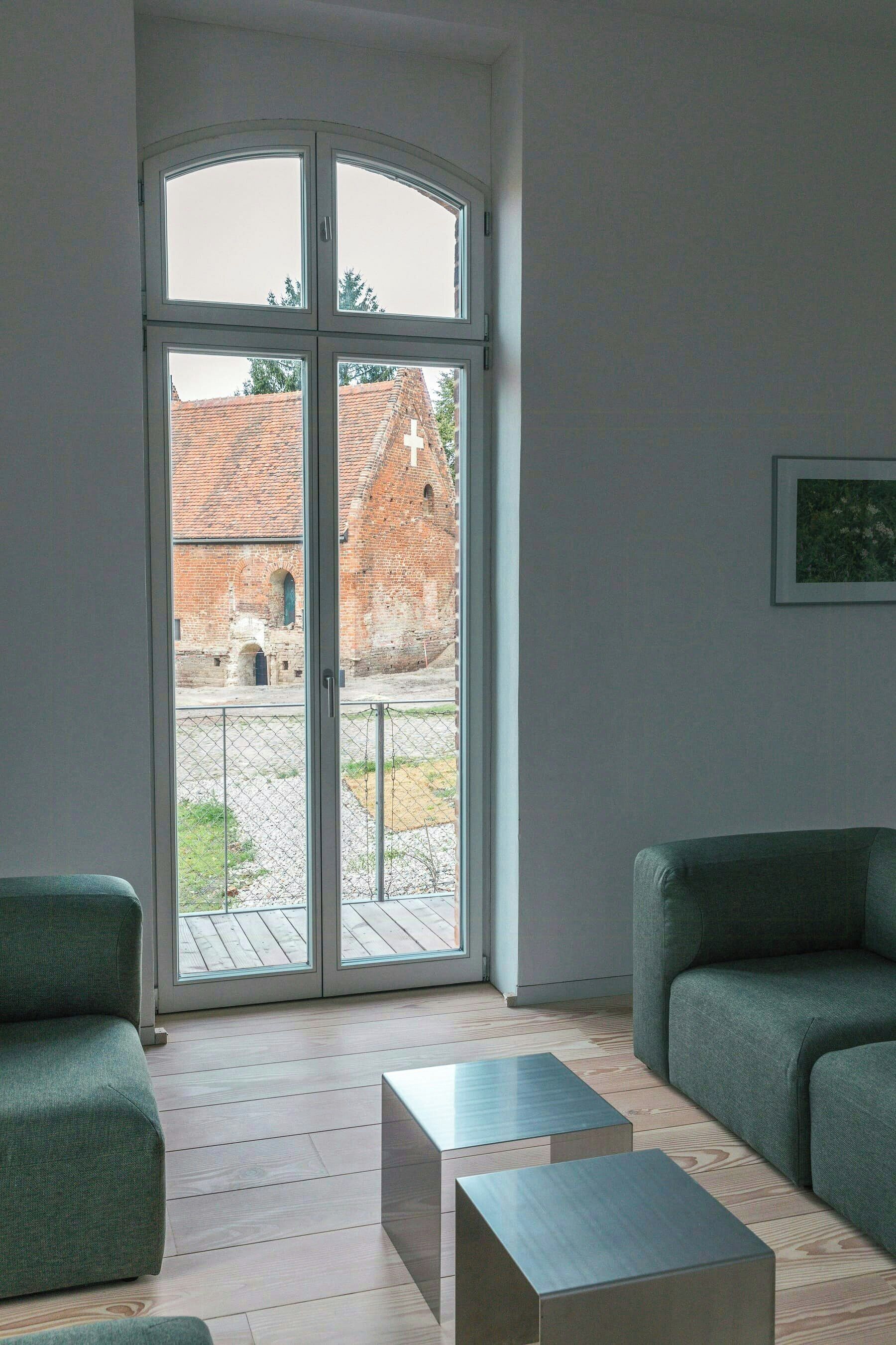 Una habitación con un amplio ventanal corredero, dos sofás verdes y una mesita.