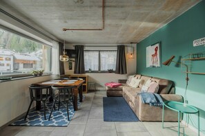 Ein gemütliches Wohnzimmer mit einer Couch, einem Esstisch mit Stühlen, einem kleinen Couchtisch und Blick auf einen Berg durch ein großes Fenster.