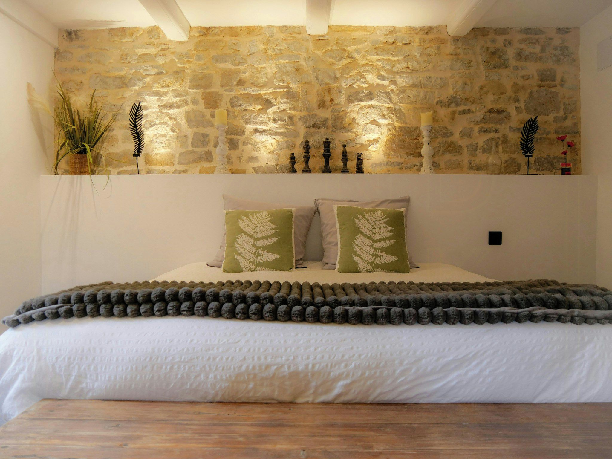 A bedroom with a stone wall, a bed with white bedding, and decorative pillows.