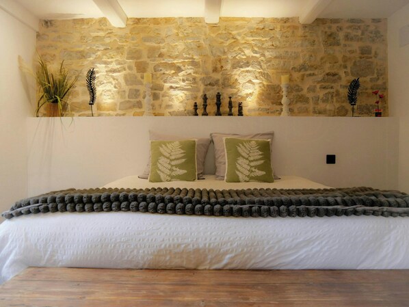 A bedroom with a stone wall, a bed with white bedding, and decorative pillows.