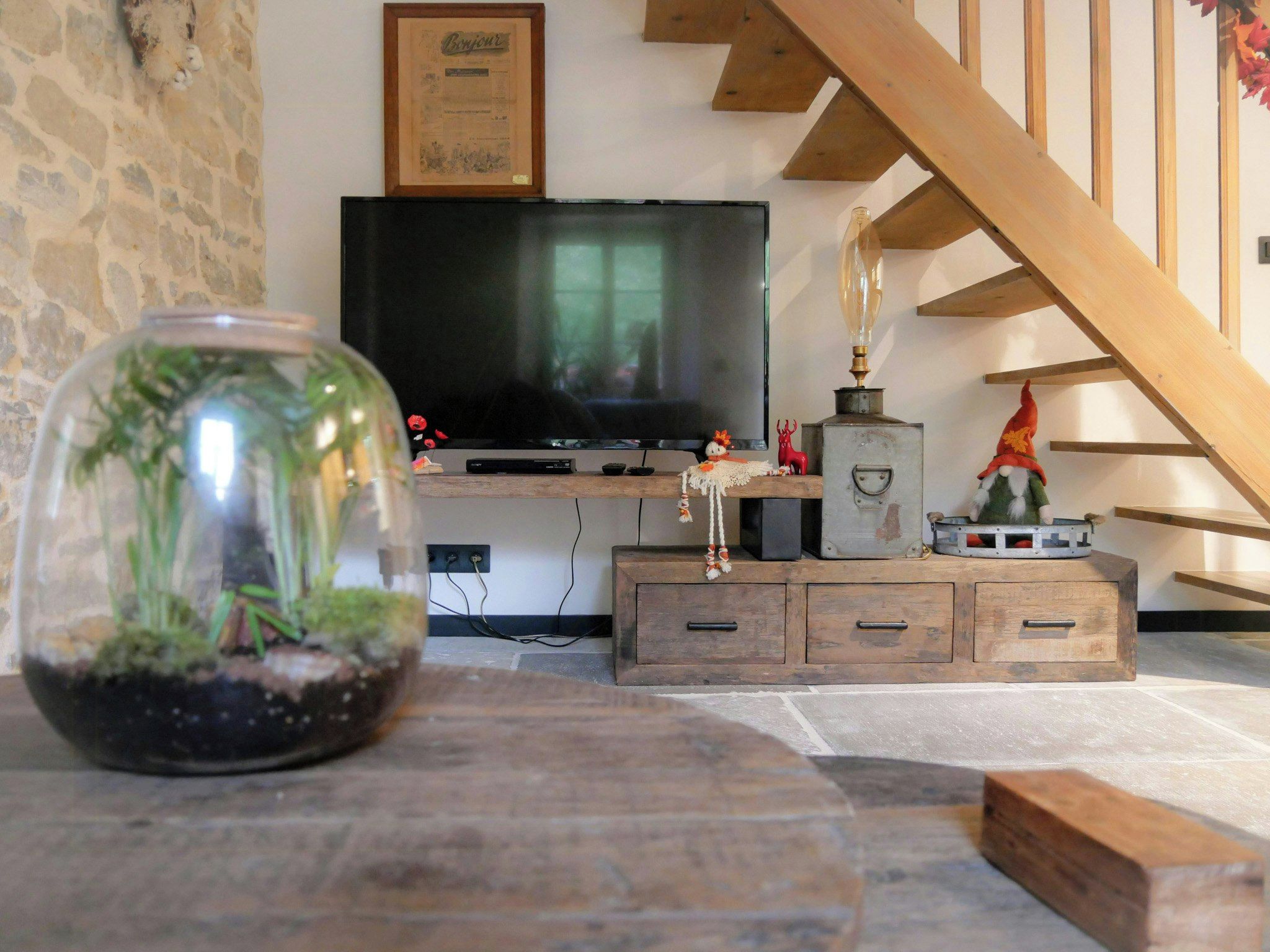 Una sala de estar con televisor, un terrario de vidrio decorativo y una escalera de madera.