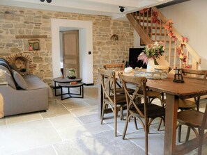 A rustic interior with a stone wall, a wooden dining table, and a staircase with autumn decorations.