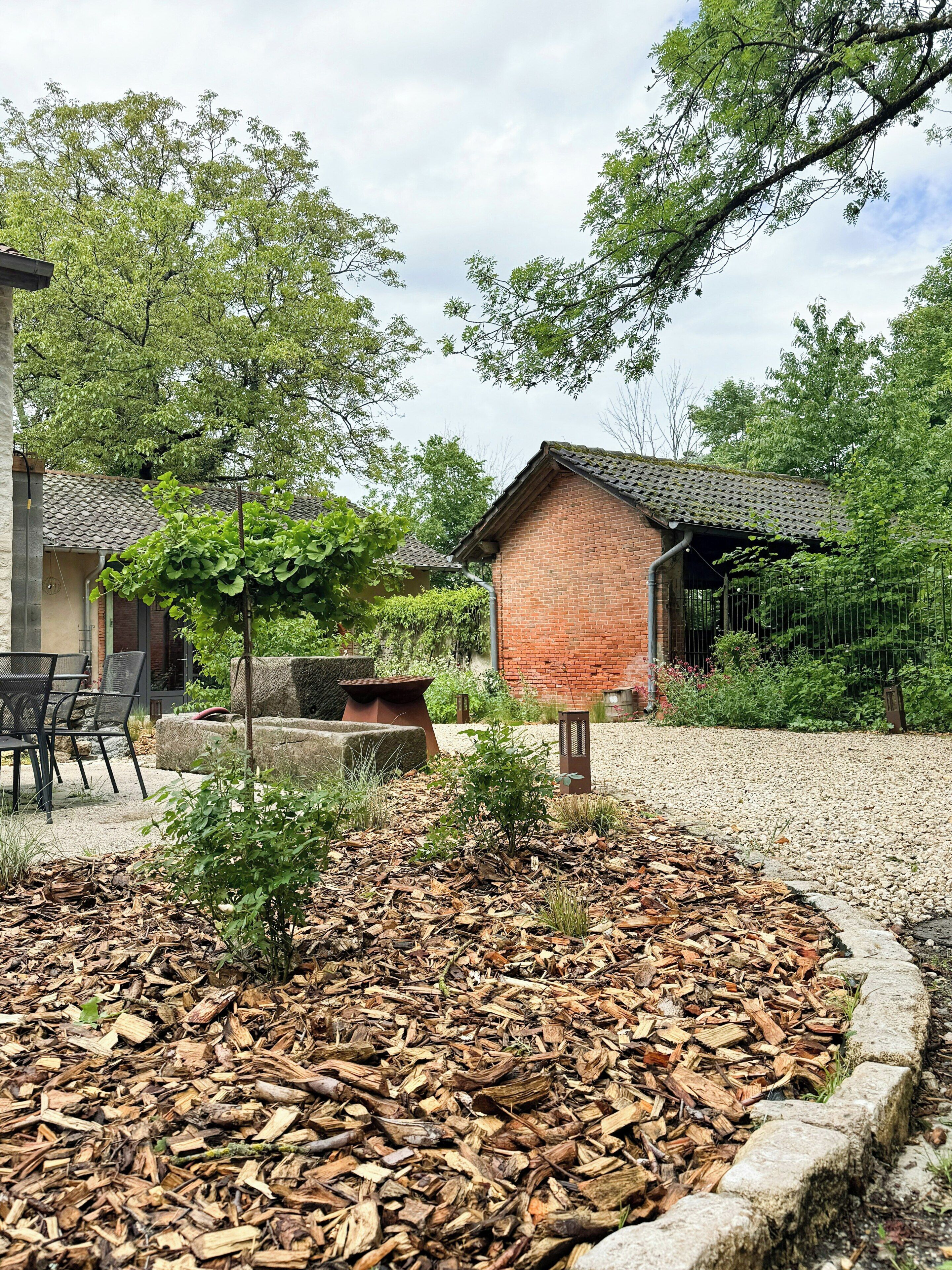 Un espace jardin agrémenté d’une structure en briques, de sièges extérieurs et d’un chemin de gravier.