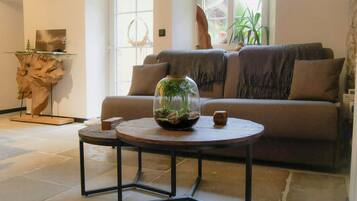 A living room with a sofa, a round table with a glass dome containing plants, and a decorative wooden piece on a stand.