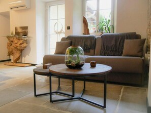 A living room with a sofa, a round table with a glass dome containing plants, and a decorative wooden piece on a stand.