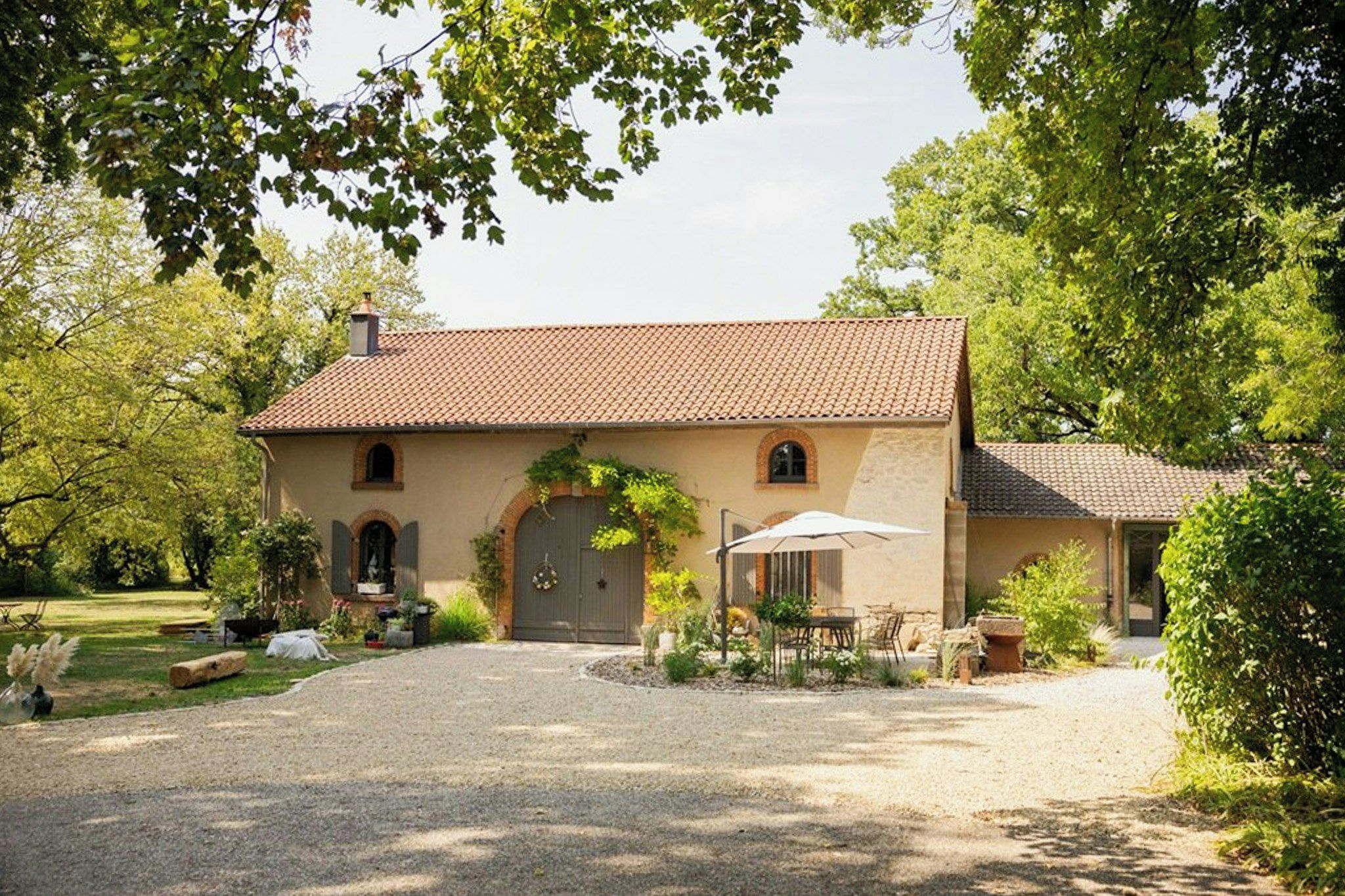 A two-story house with a gravel driveway, a covered patio, and a garden with various plants and a bench.
