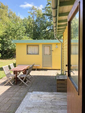 A yellow mobile home with a patio area, a table with chairs, and a door leading to a covered porch. - Swedish-inspired home in Odden's forest (Sjællands Odde)