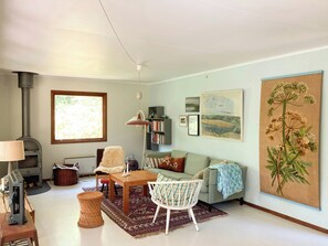 A living room with a fireplace, a sofa, a coffee table, a lamp, a bookshelf, and a large window. - Swedish-inspired home in Odden's forest (Sjællands Odde)