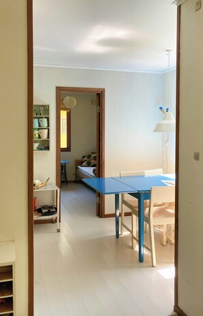 A room with a blue table and chairs, a white lamp, and a wooden door frame. - Swedish-inspired home in Odden's forest (Sjællands Odde)