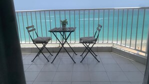 Ein Balkon mit Blick auf den Ozean, zwei Stühle, ein kleiner Tisch und ein Blumentopf.